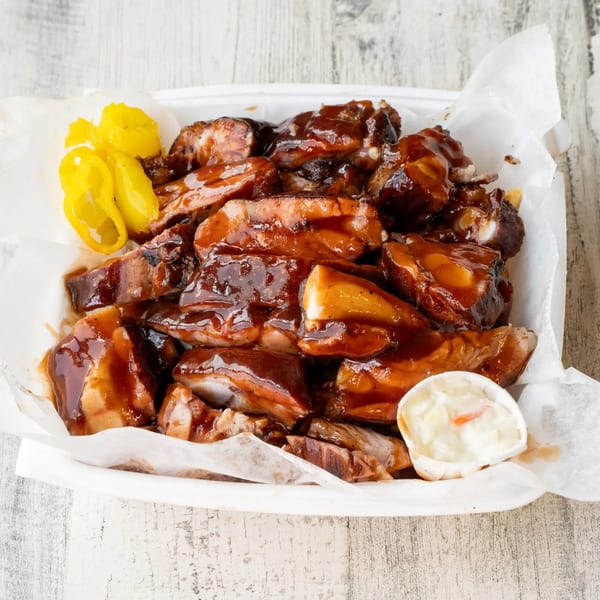 No Sauce AZ Smokehouse BBQ ribs with sauce, yellow peppers, and coleslaw in a white container.