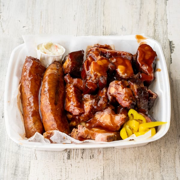 No Sauce AZ Smokehouse BBQ platter with sausages, saucy brisket, coleslaw, and pickled peppers.