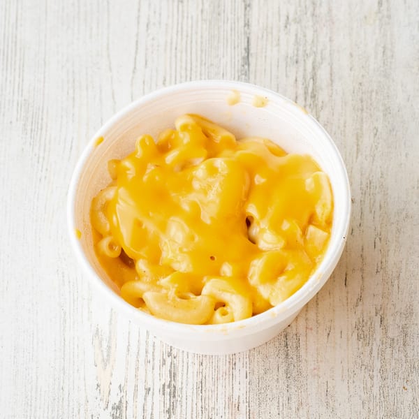 A white bowl filled with creamy, orange mac and cheese on a rustic white wooden surface.