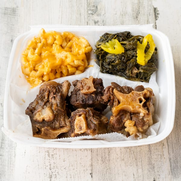 No Sauce AZ Smokehouse oxtails, mac and cheese, and collard greens with pickled peppers in a takeout container.
