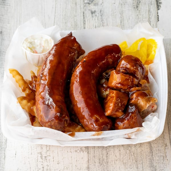 No Sauce AZ Smokehouse BBQ platter with two sausages, burnt ends, fries, coleslaw, and pickled peppers.