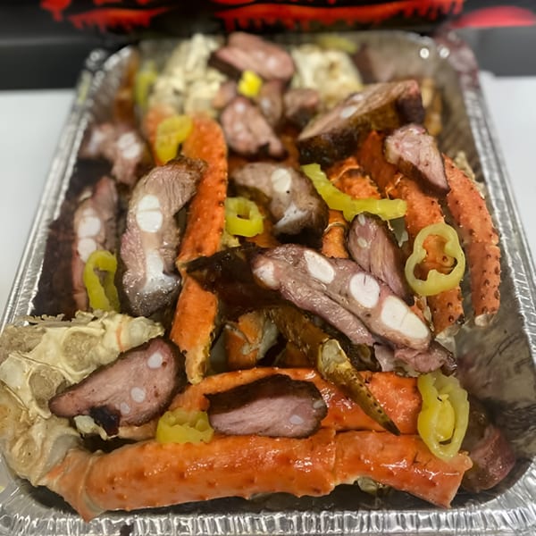 No Sauce AZ Smokehouse BBQ platter with crab legs, sliced meat, and yellow peppers in a foil pan.
