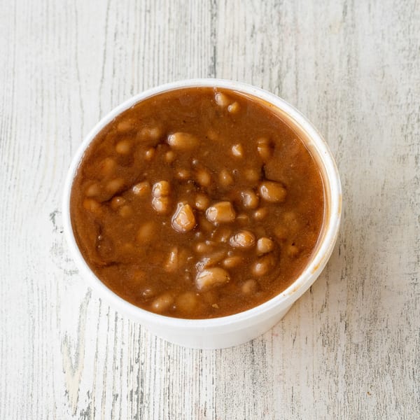 A white bowl filled with No Sauce AZ Smokehouse baked beans on a rustic white wooden surface.